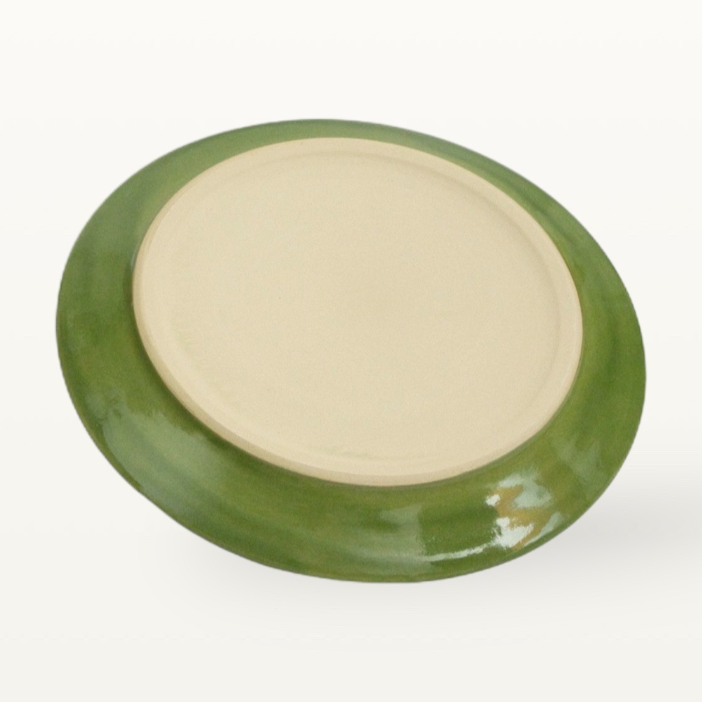 Unterseite eines gruenen, handgefertigten Tellers, unglasierter heller Scherben auf der Stellflaeche